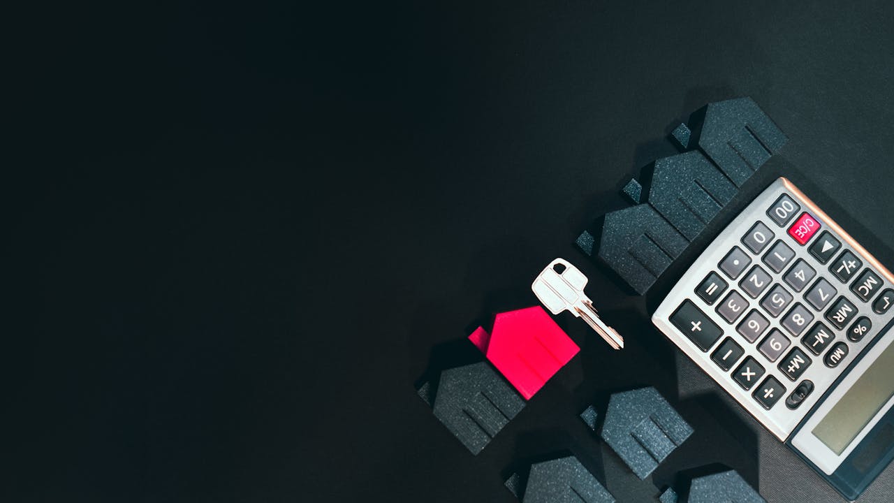 why-choose-us-02 Real estate concept image featuring a calculator, houses, and a key on a black background.